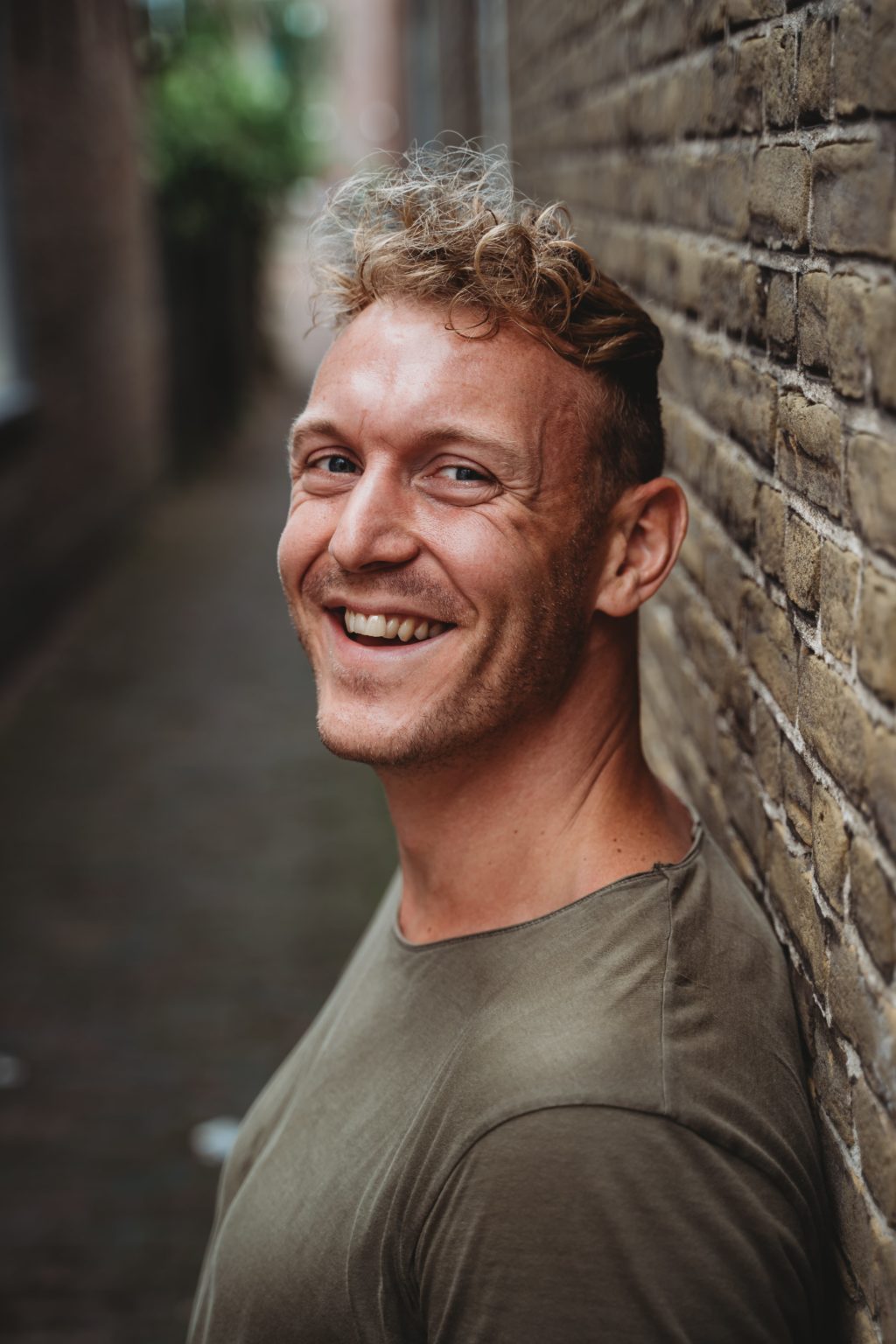 Jonathan Bouter, coach in Lelystad, lachend tegen een bakstenen muur