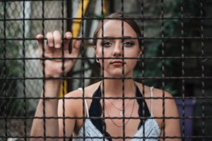 Vrouw die door een metalen hek kijkt, metafoor voor gevangen zitten in eigen gedachten en overtuigingen