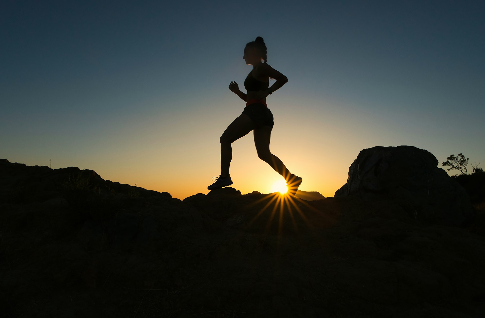 Hardlopende vrouw als silhouet tegen de opkomende zon