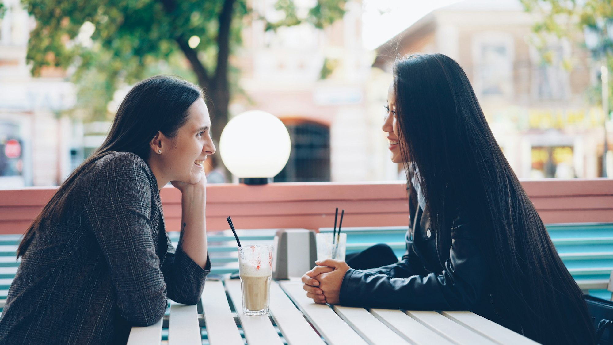 Twee vrouwen leunen over een tafeltje naar elkaar toe in gesprek