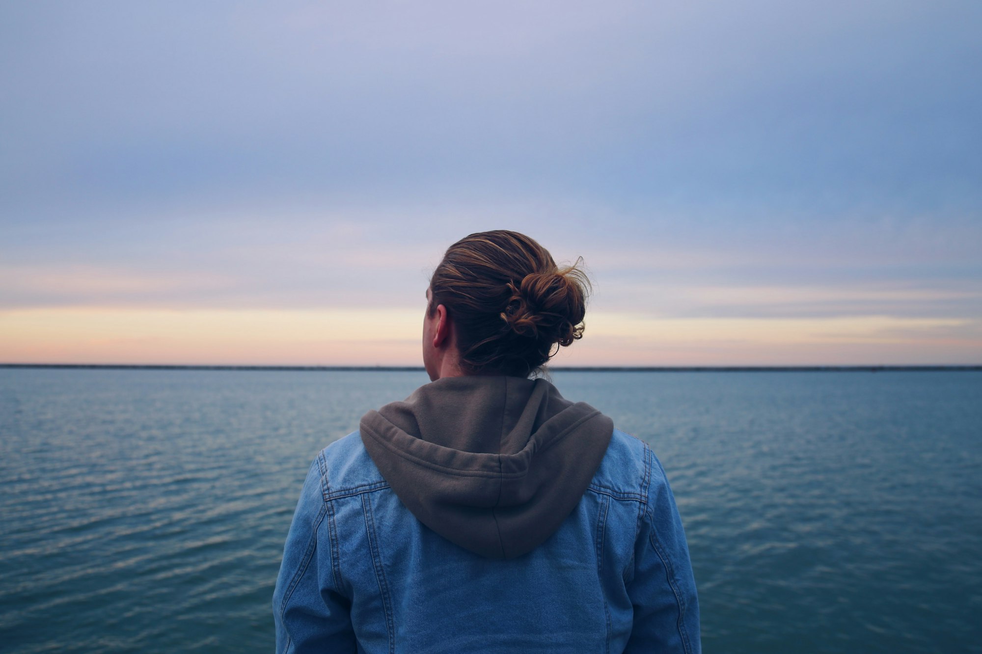Vrouw staat met haar rug naar ons en kijkt over de zee naar de horizon