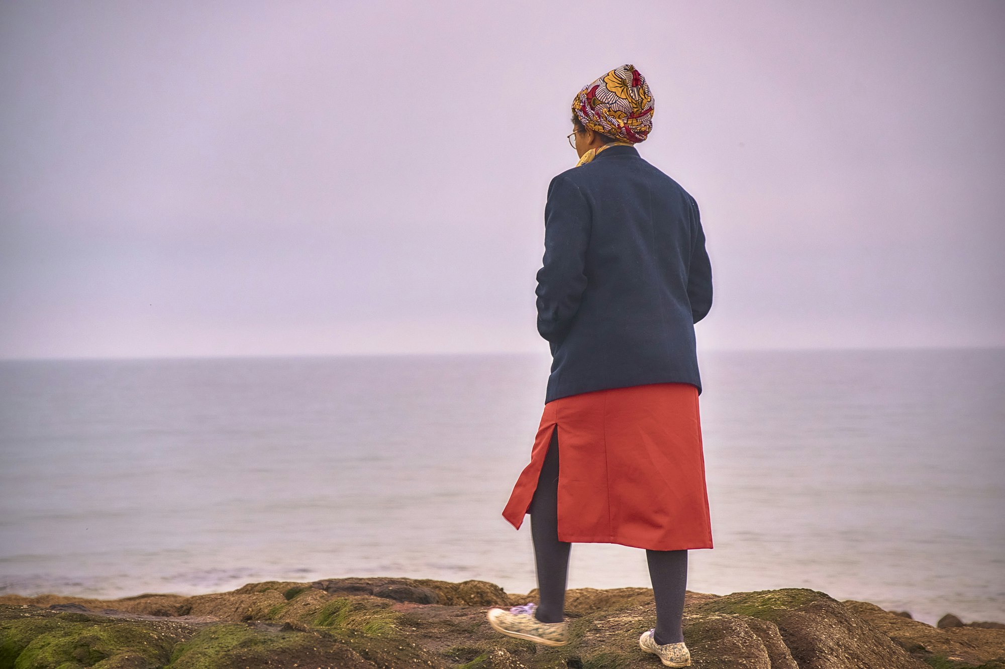Vrouw staat aan de waterkant en kijkt naar een roze horizon