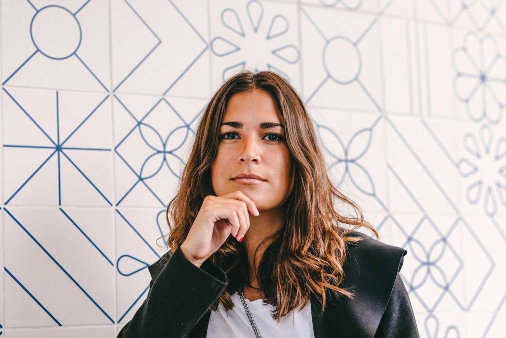 Vrouw in blazer met rustige, directe blik, hand onder de kin