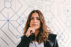 Vrouw in blazer met rustige, directe blik, hand onder de kin