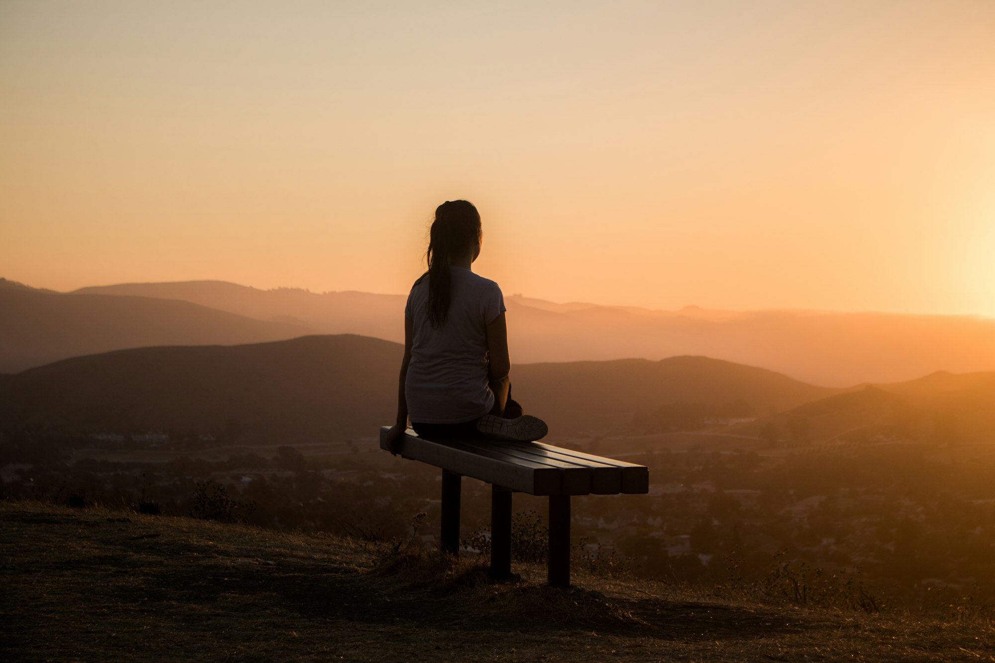 Vrouw zit op een bankje en kijkt uit over bergen bij zonsopgang
