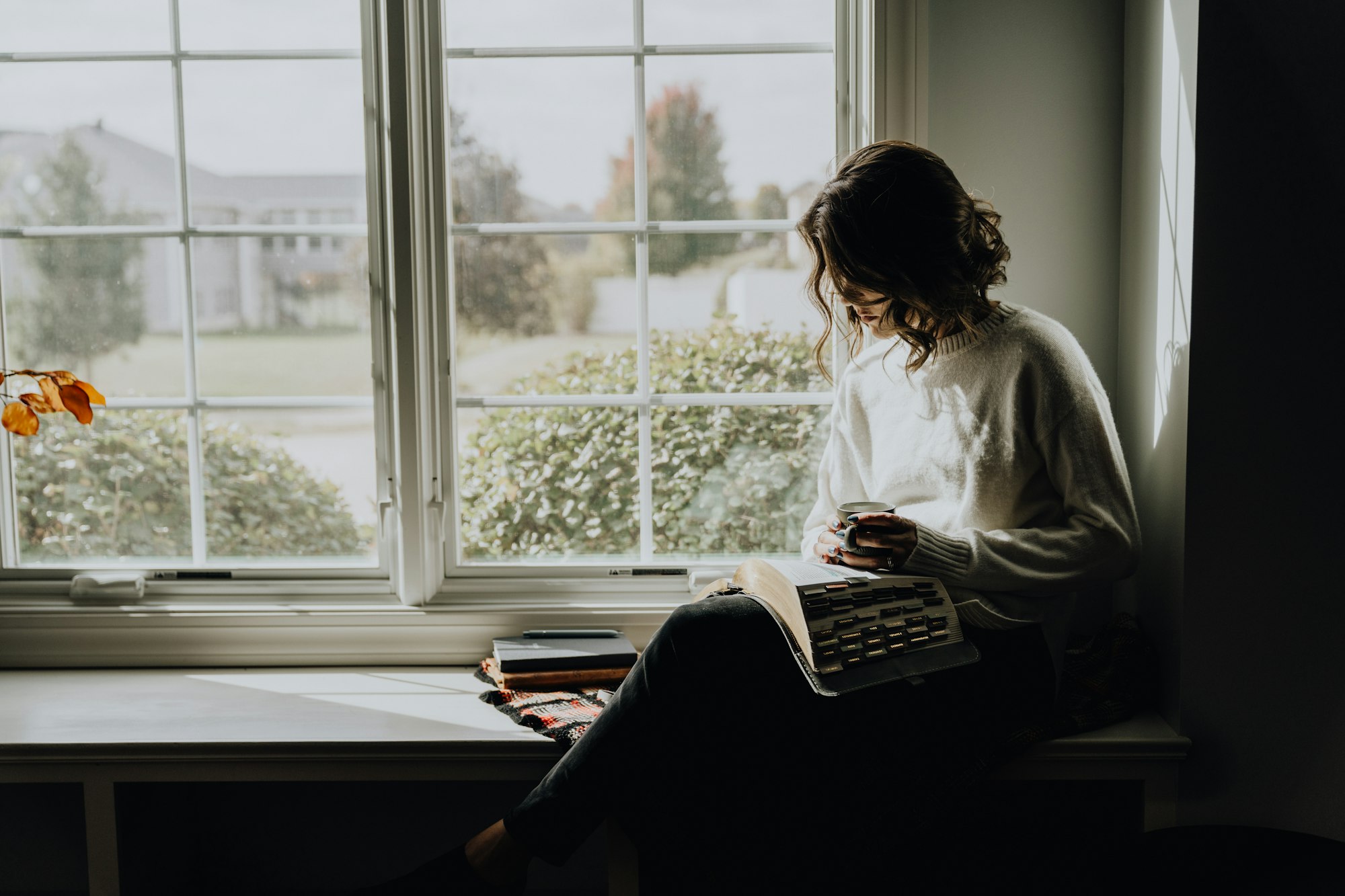 Vrouw zit in een vensterbank te lezen bij daglicht