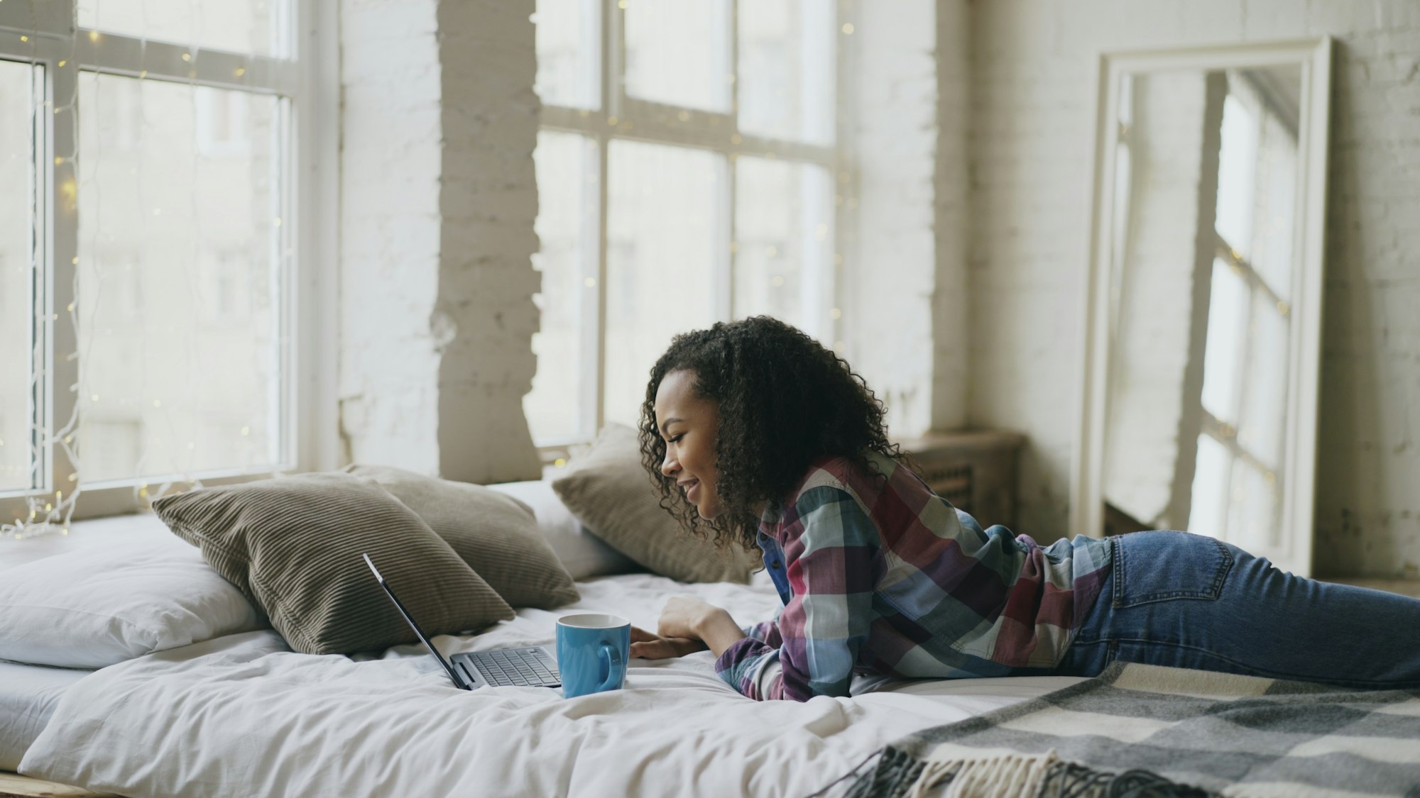 Vrouw werkt met haar laptop op bed bij het raam