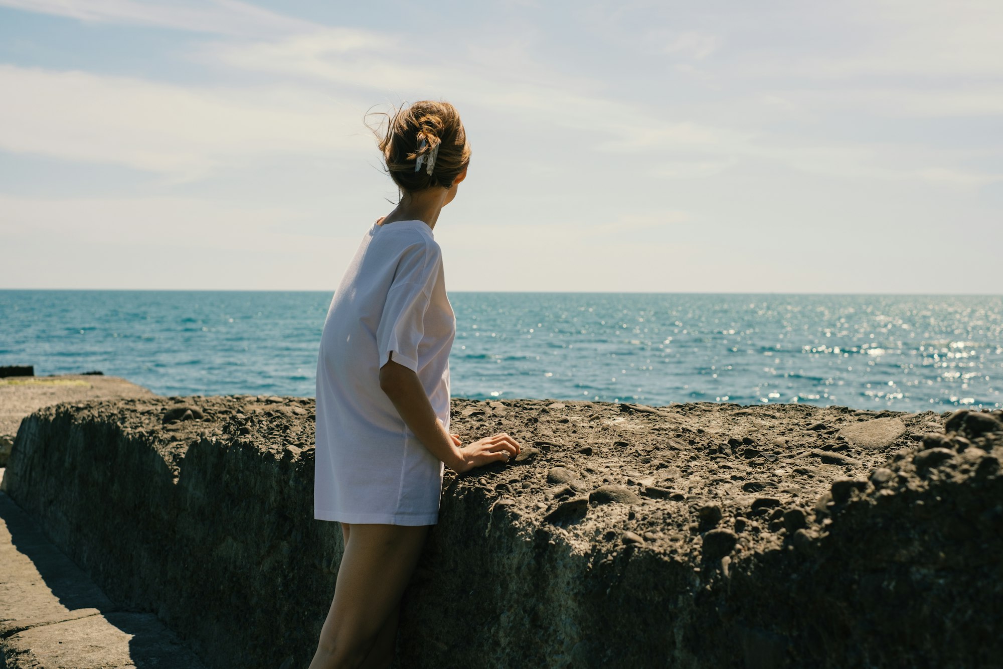 Vrouw staat op een rots aan zee en kijkt naar de horizon