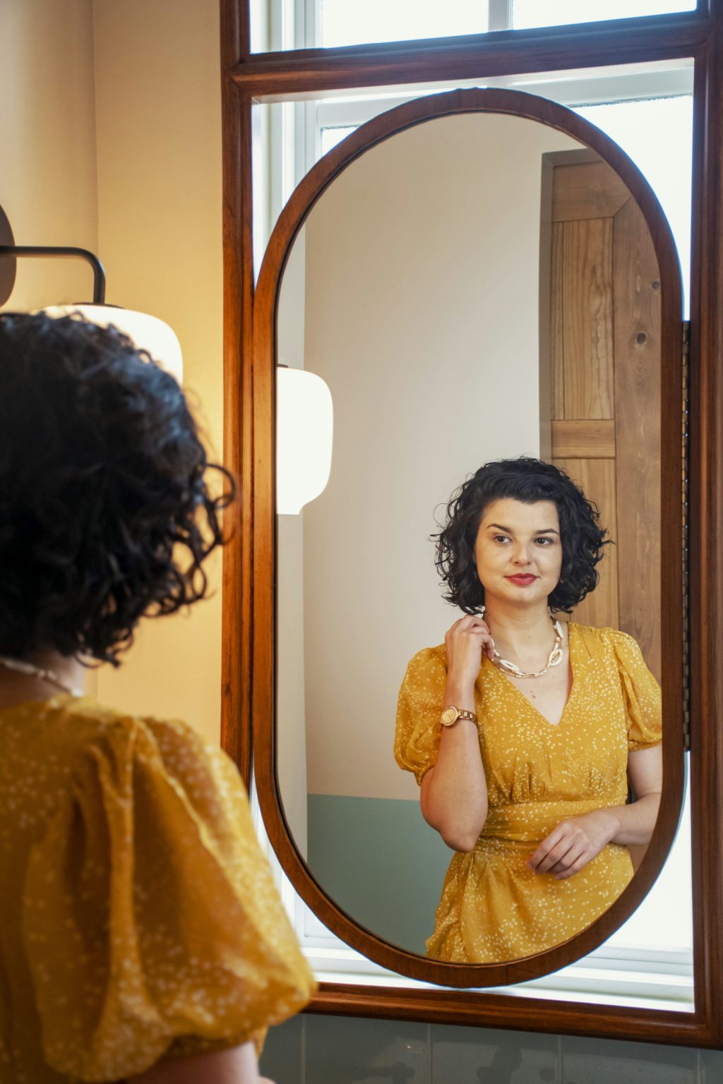 Vrouw in een gele jurk lacht naar haar eigen spiegelbeeld