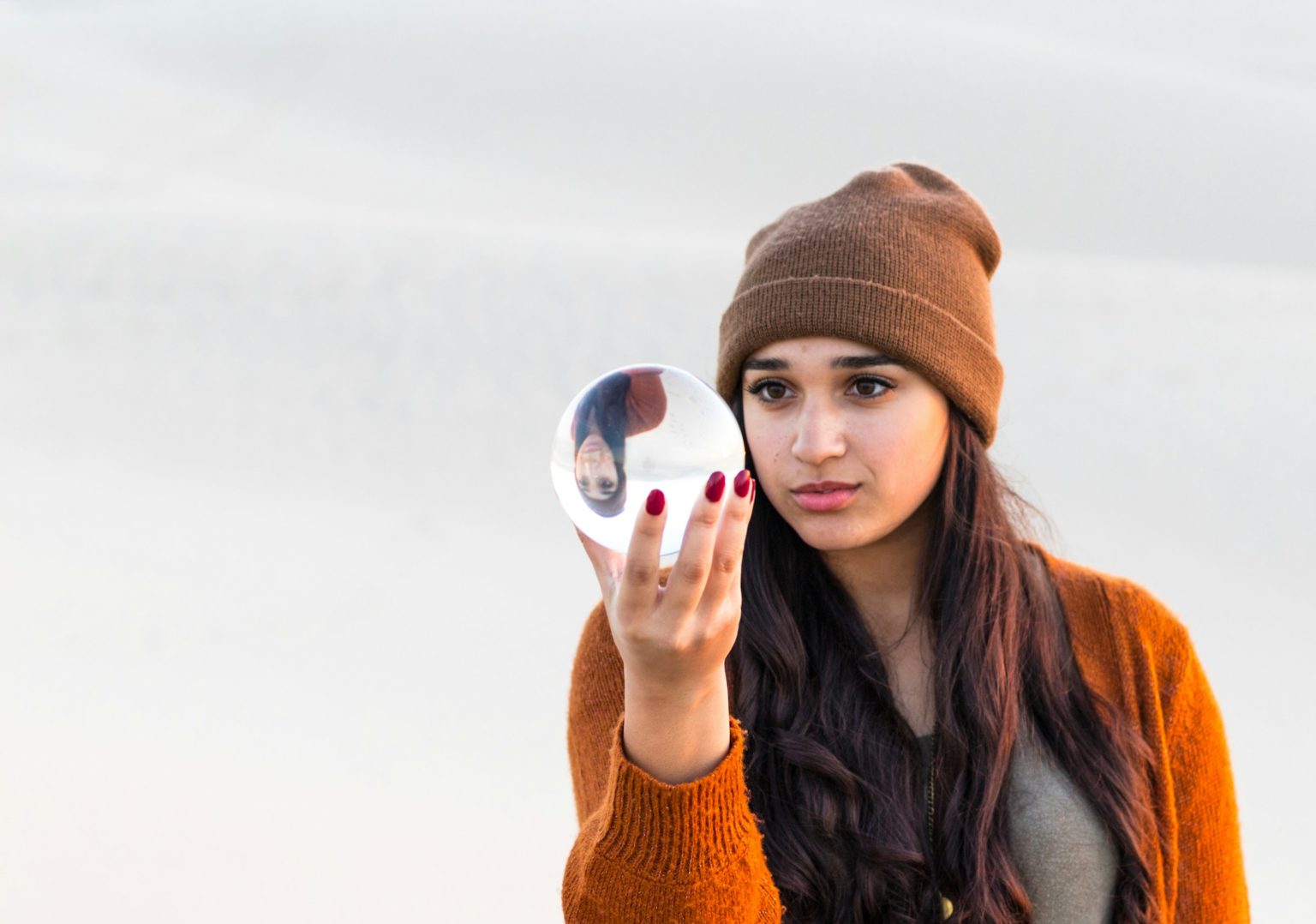 Vrouw met muts houdt een glazen bol omhoog en kijkt erin
