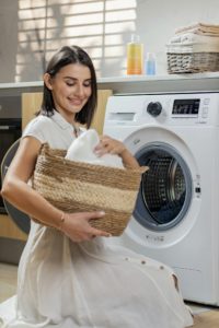 Lachende vrouw met een wasmand vol was bij de wasmachine