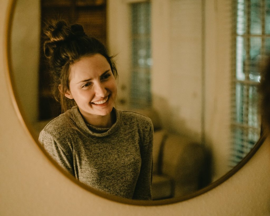 Vrouw glimlacht naar haar spiegelbeeld in een ronde spiegel