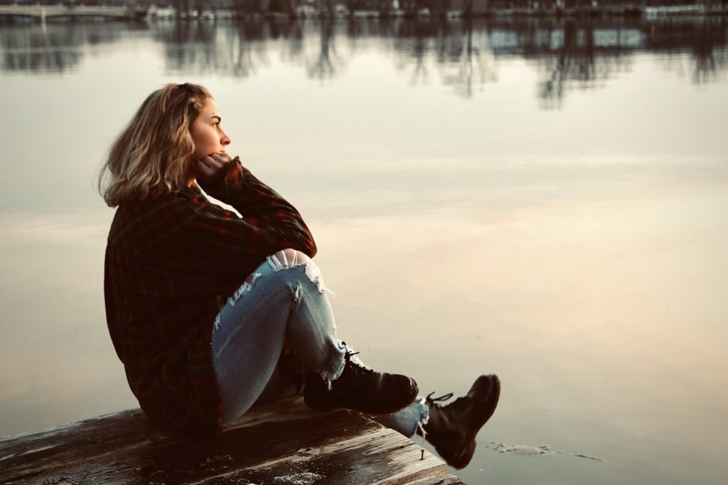 Vrouw zit nadenkend op een muurtje bij zonsondergang