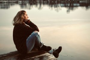 Vrouw zit nadenkend op een muurtje bij zonsondergang