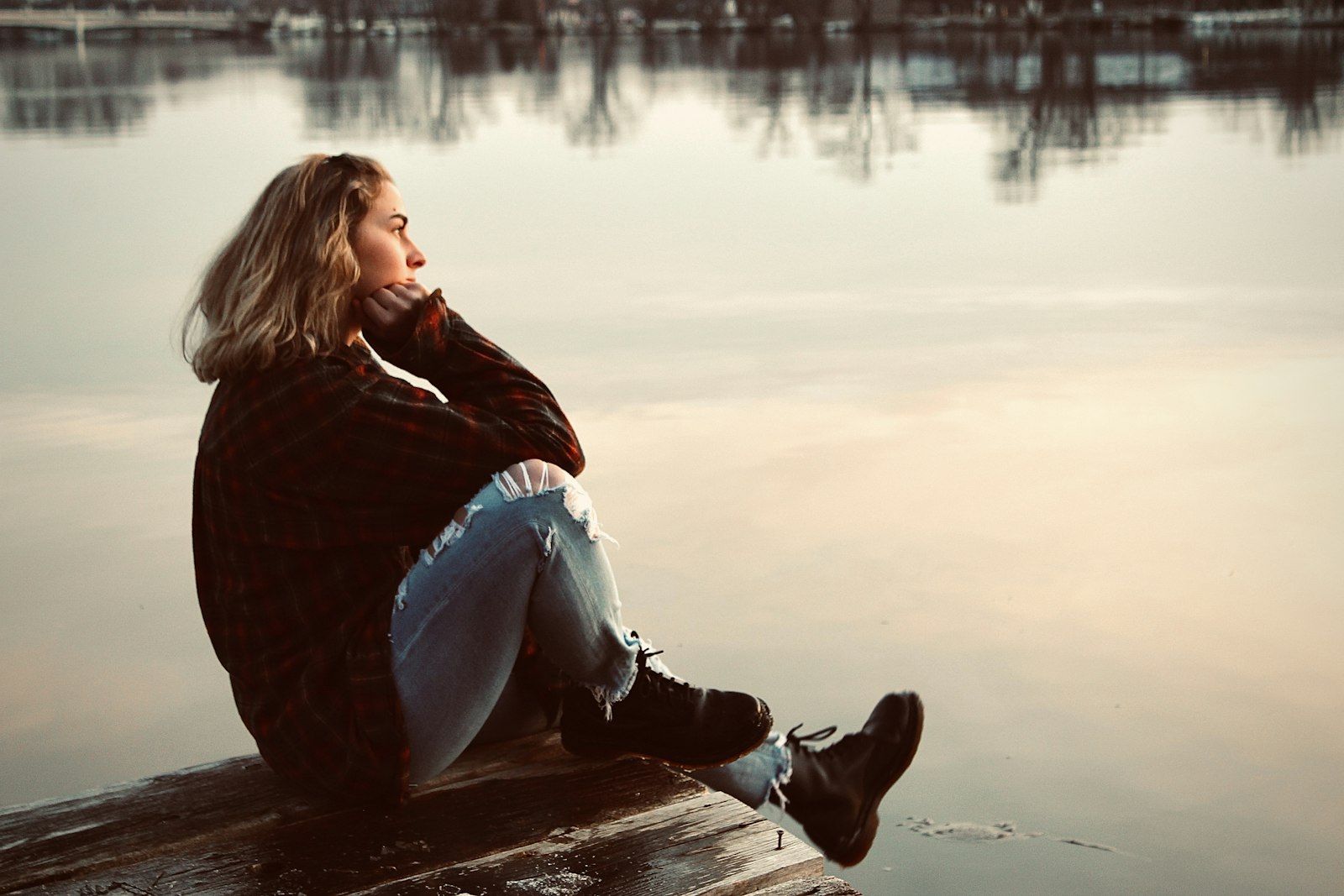Vrouw zit nadenkend op een muurtje bij zonsondergang