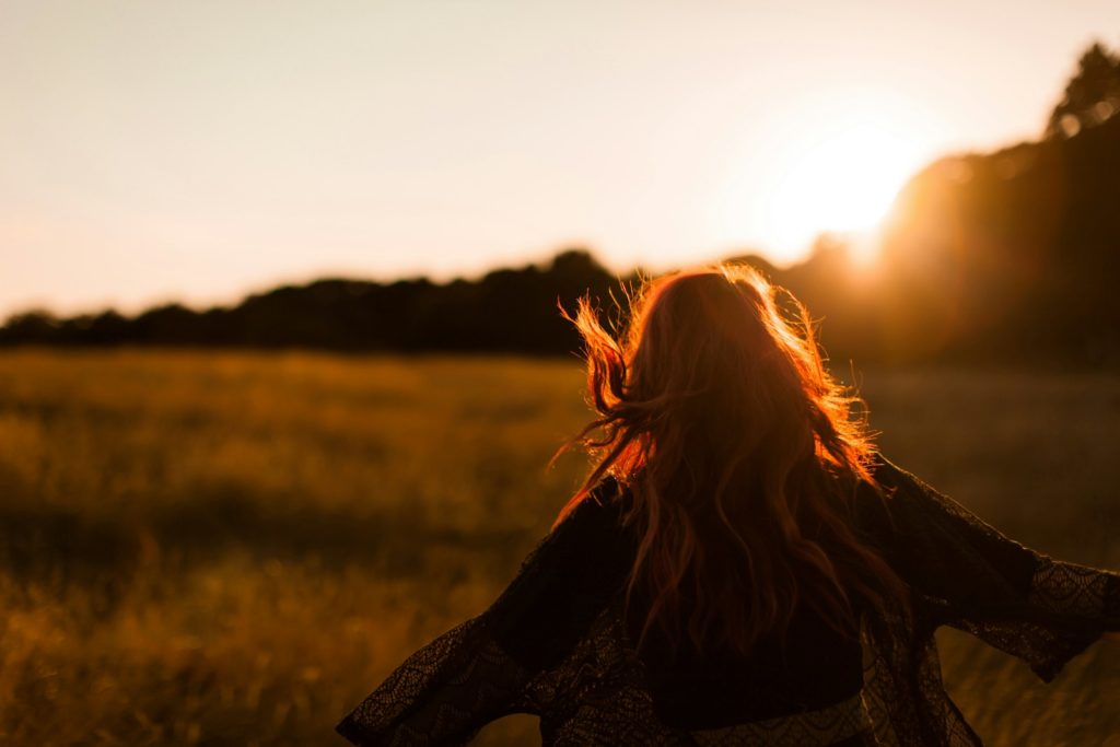 Vrouw staat vrij in een veld in het avondlicht