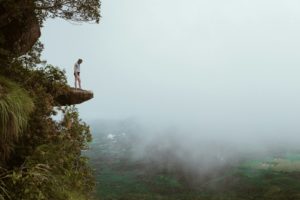 Vrouw staat aan de rand van een rots boven de mist