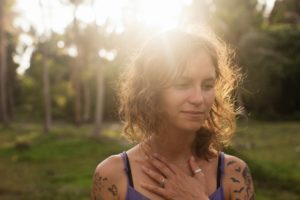 Vrouw in de zon met haar ogen dicht en haar hand op haar borst