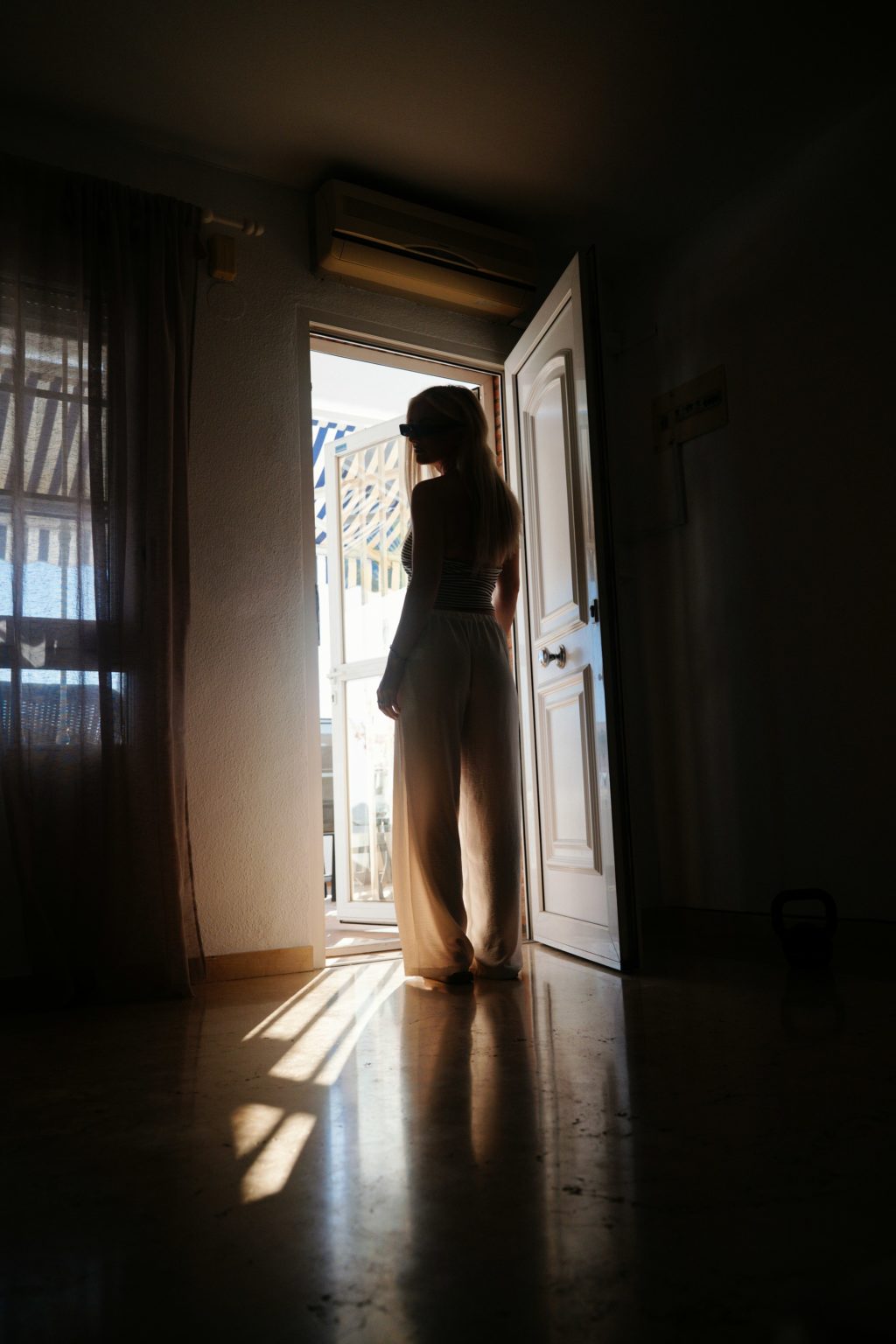 Vrouw staat in een donkere kamer bij een open deur vol licht