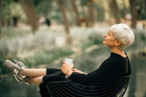 Vrouw zit ontspannen buiten in een stoel met haar benen omhoog en een kop koffie in haar hand