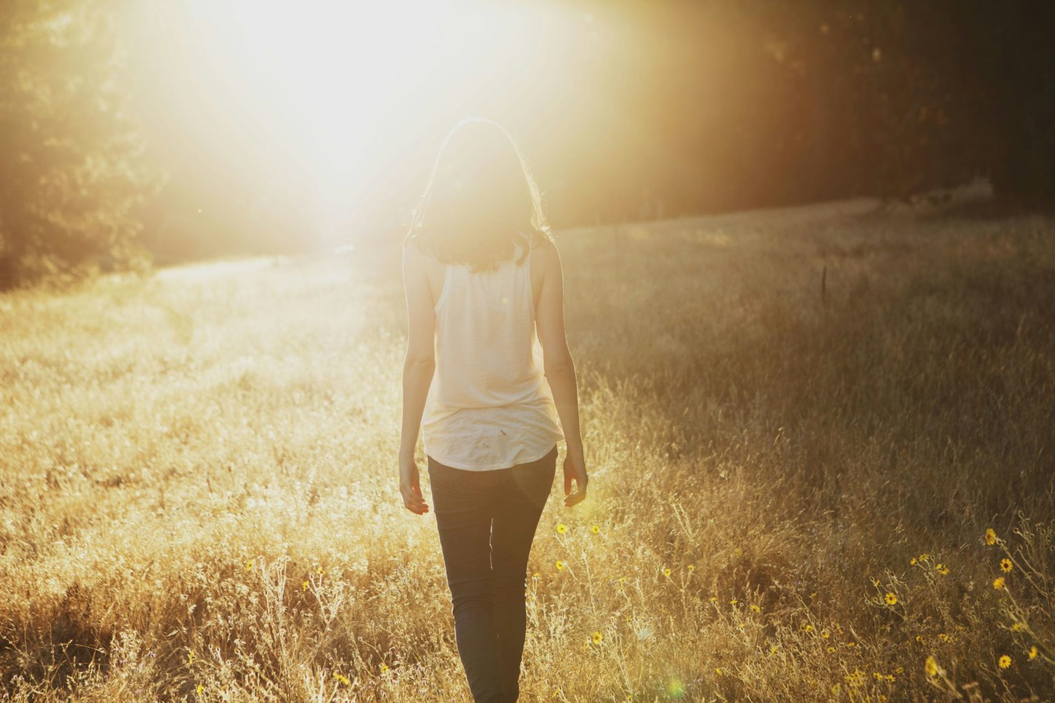Vrouw loopt door een veld richting het zonlicht