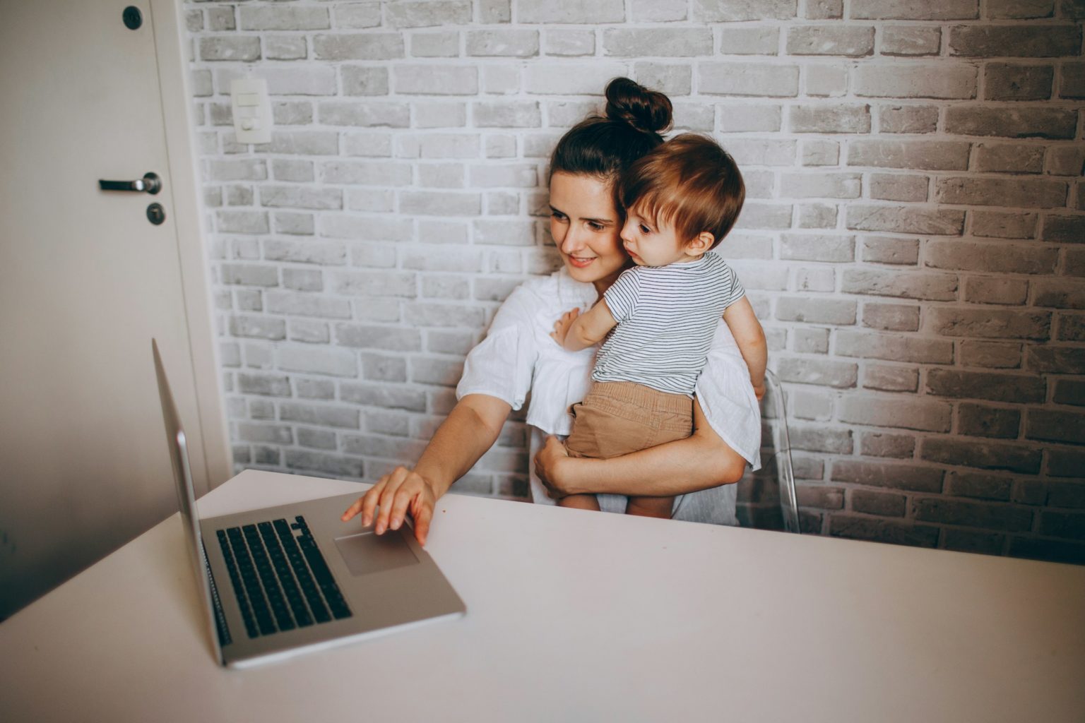 Moeder aan de laptop met haar kind op de arm