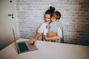 Moeder aan de laptop met haar kind op de arm