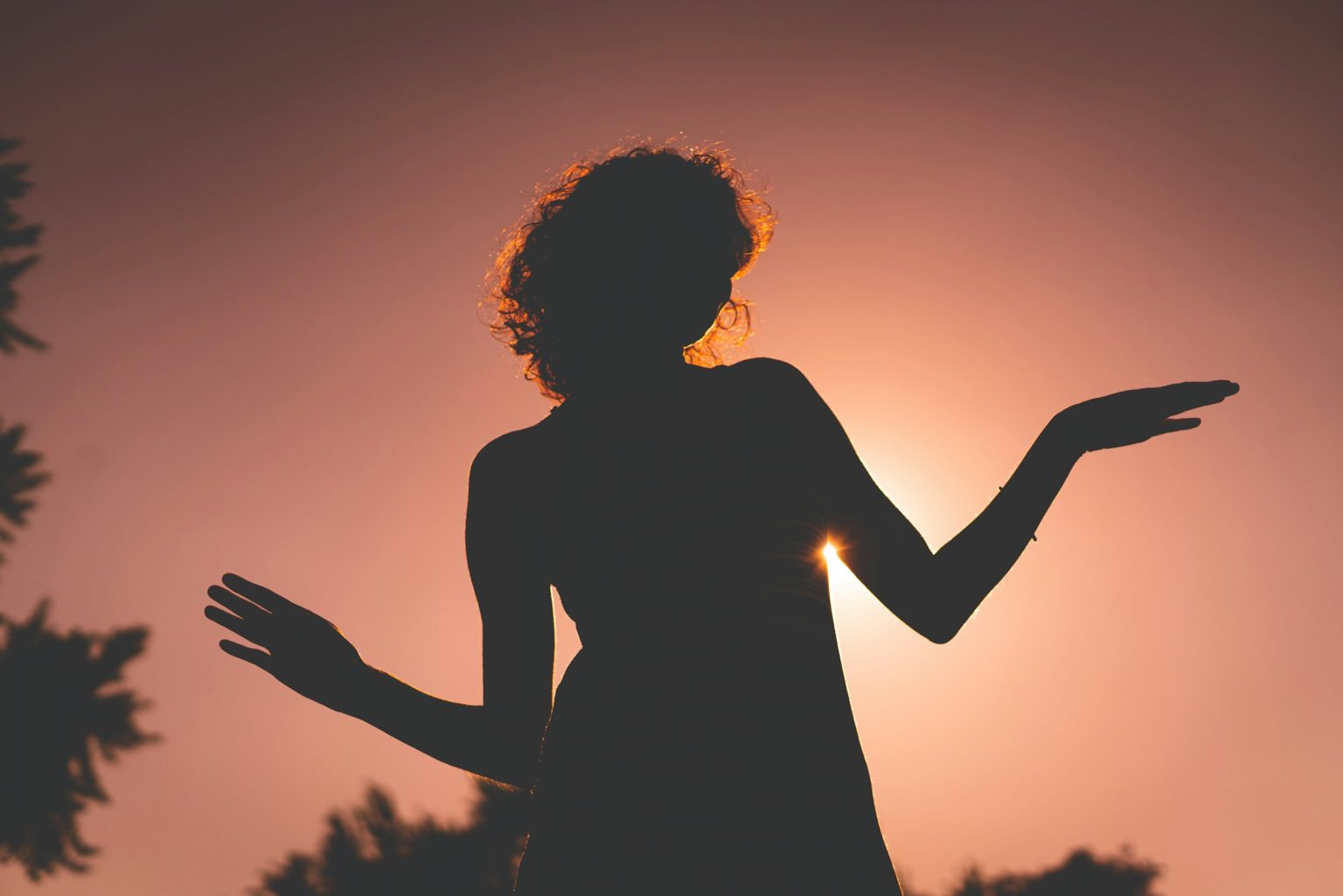Silhouet van een vrouw met open handpalmen naar boven in het avondlicht