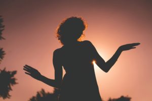 Silhouet van een vrouw met open handpalmen naar boven in het avondlicht