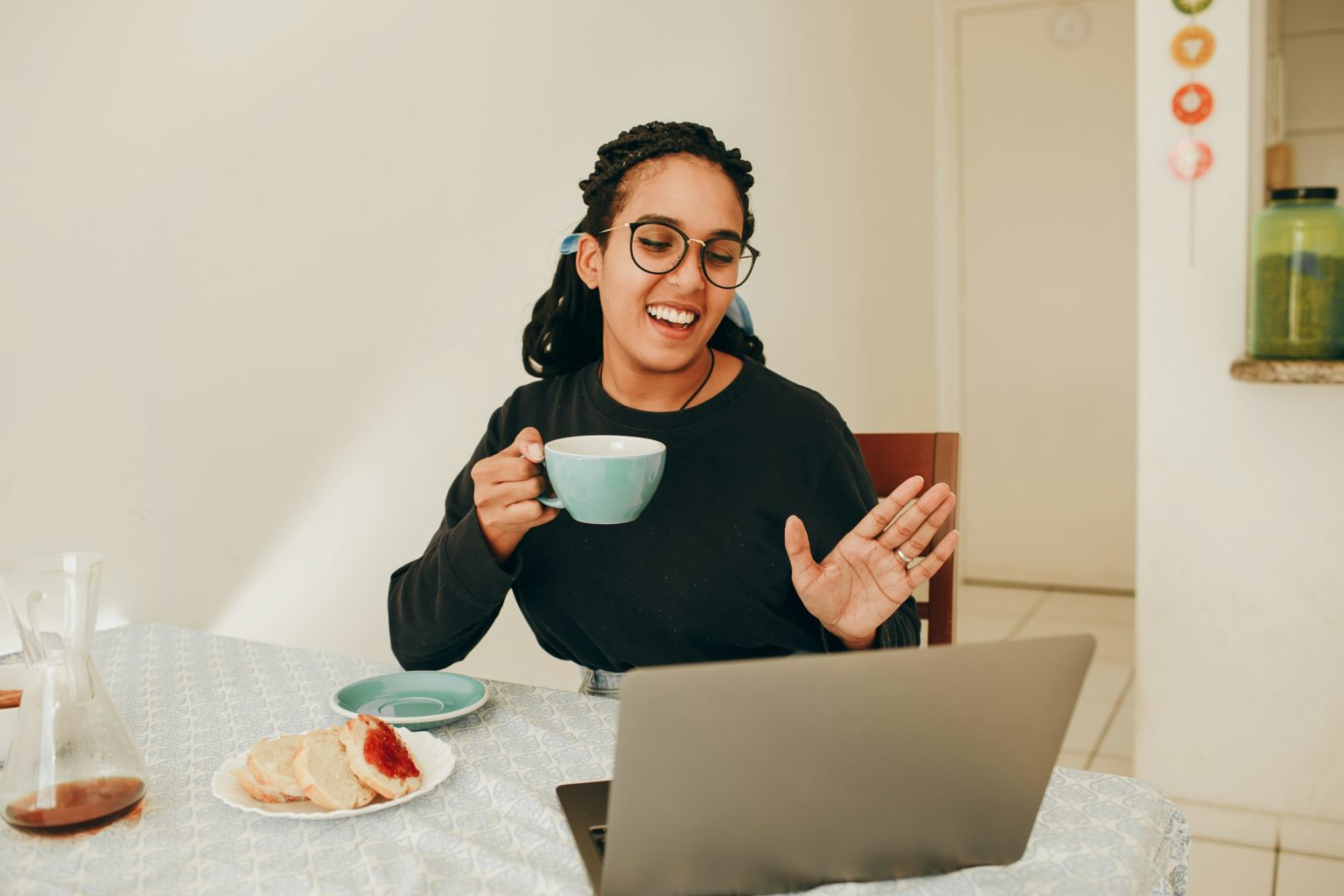 Vrouw aan tafel met een kop thee voor haar laptop, in gesprek tijdens een sessie via Zoom